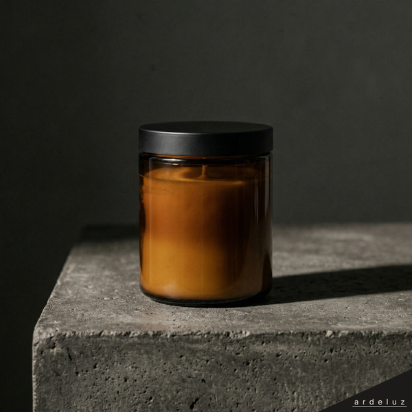 ardeluz BRASA candle in amber glass jar with matte black lid on dark concrete